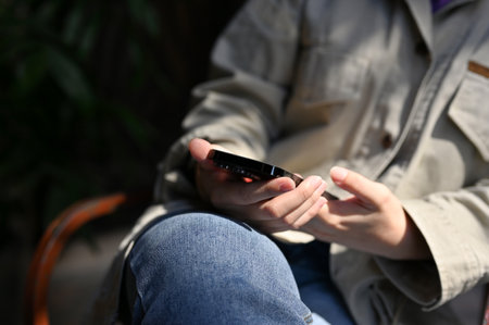 A female hands holding a smartphone, using her modern mobile phone while relaxing at the coffee shop. cropped imageの写真素材