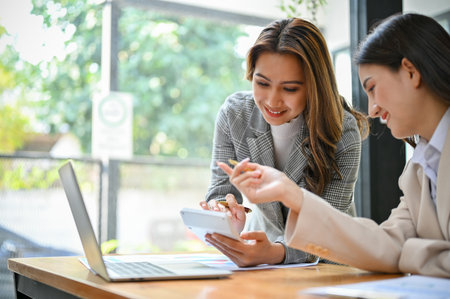 Two professional and teamwork millennial Asian businesswomen or female accountants working together, analyzing business sales report, calculating financial income.の写真素材