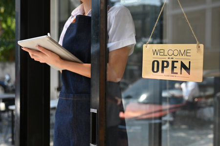 cropped image, Young Asian female barista or coffee shop owner in apron stands at her coffee shop's...