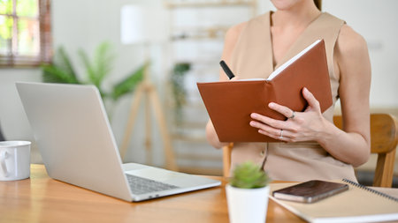 cropped image, Beautiful millennial Asian businesswoman or female boss working at her desk, taking notes or making lists on her notebook.の写真素材