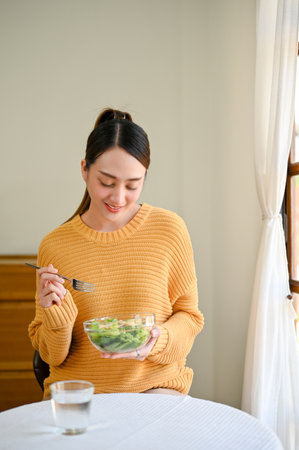 Portrait, A beautiful Asian woman is on diet, enjoys eating salad vegetables mix for her breakfast in her dining room. healthy lifestyle conceptの写真素材