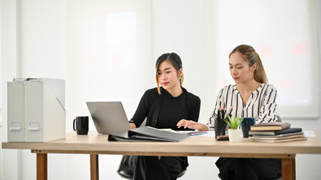 Two focused and professional Asian businesswomen working in the office together, managing their...
