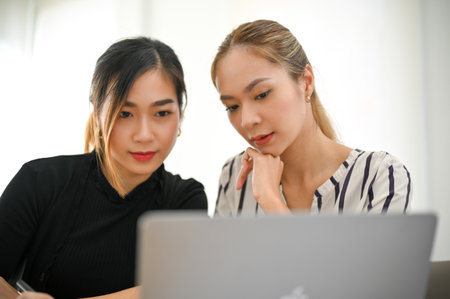 Two smart and professional millennial Asian businesswomen focusing on a project, looking at laptop...