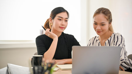 Two gorgeous and professional millennial Asian businesswomen concentrating on their project, looking...