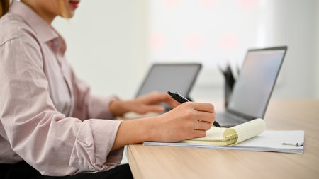 cropped shot, Attractive millennial Asian businesswoman working at her office desk, taking notes or...