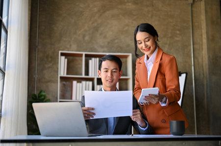 Two professional millennial Asian financial analysts or consultants working on sales and financial investment report together in the office.の写真素材