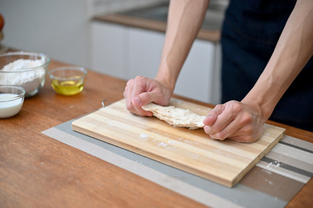 Close-up hand image of a male baker kneading raw dough, preparing dough for his pastry, making...