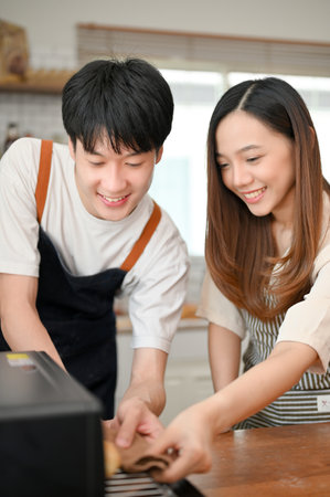 Portrait, Happy and lovely young Asian couple putting tray in the oven, enjoy baking in the kitchen together.の写真素材
