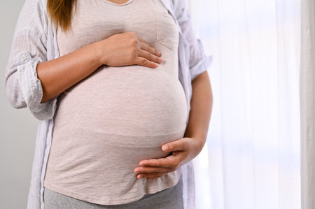 A pregnant woman in comfortable clothes touching her big belly with love and care, feeling her baby...