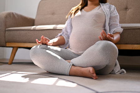 Cropped image of a happy and relaxed Asian pregnant woman in comfortable clothes meditating in her living room, lotus pose, concentrating breath.の写真素材