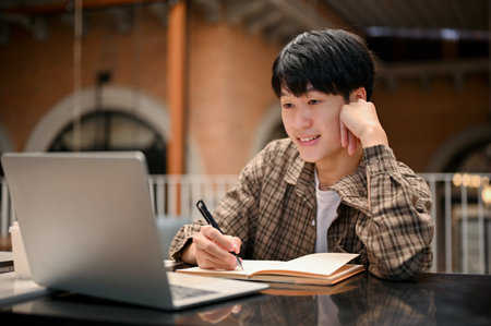Happy and smart young Asian male college student remote working at the cafe, doing his school...