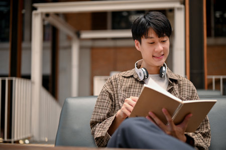 Happy and relaxed young Asian man in casual clothes reading a book in the cafe. hobby and leisure conceptの写真素材