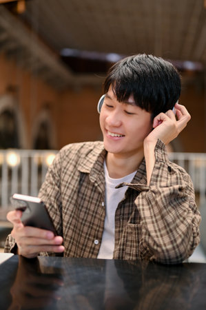 Portrait, Happy and cheerful young Asian man sits at the cafe listening to music though his...