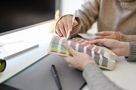 Two creative graphic designers discussing and choosing color on color palette chart for their...