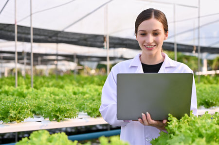 Professional Caucasian female agricultural scientist or biologist using laptop, checking hydroponic...