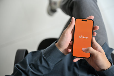 Chiang Mai, Thailand - Feb 17 2023: Top view of a man using Payoneer mobile application at his desk....