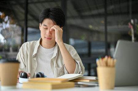 Unhappy and upset young Asian male college student sits at the coffee shop or co-working space with...