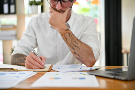 Cropped image of a thoughtful and focused Caucasian businessman working on financial data report, analyzing his business financial potential, noting something on his notebook.の写真素材