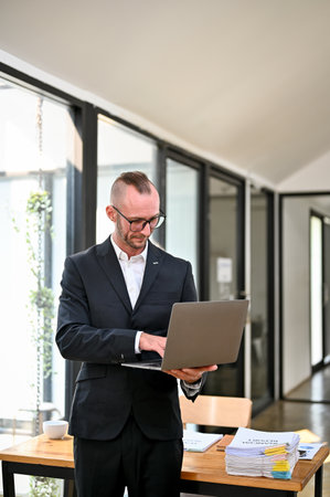 Portrait, Smart and focused Caucasian businessman or male CEO in formal business suit using portable laptop while standing in the office.の写真素材