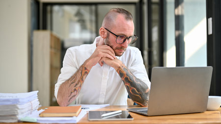 Thoughtful and focused Caucasian businessman or male business entrepreneur with tattoo on his arms...