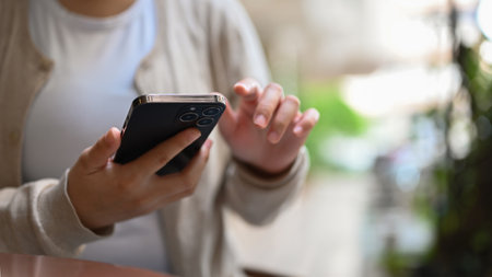 Cropped image of an Asian female in casual clothes relaxing in the city park and using her smartphone.の写真素材