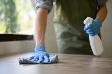 Cropped image of a man wearing rubber gloves using cleaning spray and dust cloth to clean to table, wiping the table.の写真素材