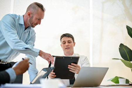 Smart and professional Caucasian businessman is talking with his colleague, looking the details on...