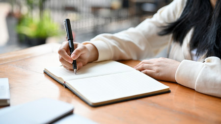 Cropped image of a young Asian female college student writing diary or noting something on her...