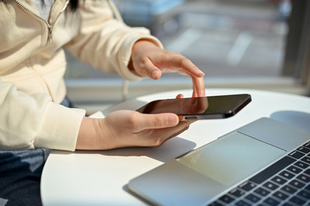 Cropped image of a woman in casual clothes using her smartphone, checking texts, sending email,...