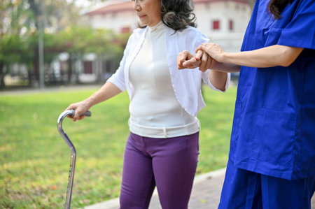 Cropped image of a caring Asian female caregiver or nurse is helping an old lady walk with a walking stick while walking together at the park. health care conceptの写真素材
