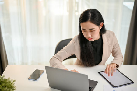Professional millennial Asian businesswoman focusing on her business tasks on laptop, using laptop at her desk in the office.の写真素材