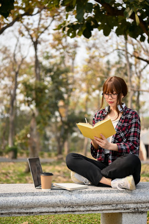 Attractive young Asian female college student in casual clothes focusing on reading a book on a...