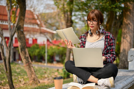 Attractive young Asian female college student focusing on her school project and using laptop on a...
