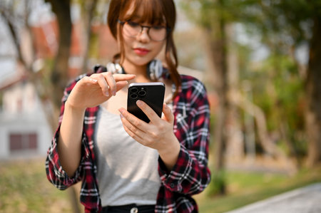 Selective focus image of a beautiful young Asian female college student using her phone at the campus park.の写真素材