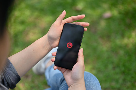 Chiang Mai, Thailand - March 16 2023: An Asian woman using Pinterest application on her mobile phone. iPhone with Pinterest logo on screen. close-up imageのeditorial素材
