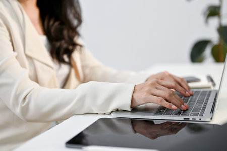 Cropped side view image, an Asian businesswoman or female office worker typing on keyboard, browsing internet, working on her project on laptop computer at her desk.の写真素材