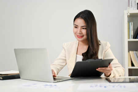 Professional and beautiful millennial Asian businesswoman or female accountant focusing on her tax reports, using laptop, working in her office.の写真素材