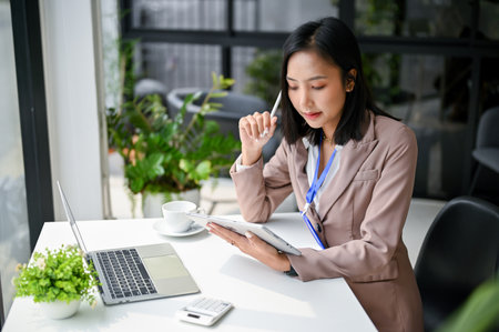 Professional and beautiful millennial Asian businesswoman focusing on her business tasks on tablet, working at her desk in the office.の写真素材
