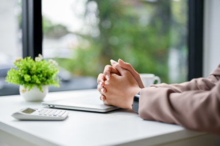 Stressed and serious businesswoman sits at her table with clasped her hands together on table. close-up imageの写真素材