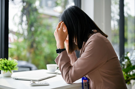 Stressed and serious millennial Asian businesswoman or female office worker sits at her desk, suffering from headache, worried about her project's deadline.の写真素材