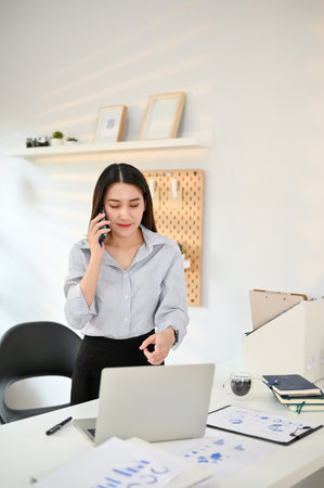 Professional and focused young Asian businesswoman or female accountant talking on the phone with her business client in her office.の写真素材