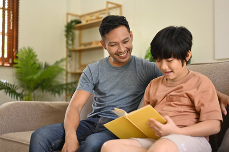 Happy and caring Asian dad is teaching his son to read a book, telling a fairytale story, or reading a cartoon together on a sofa in the living room. happy familyの写真素材