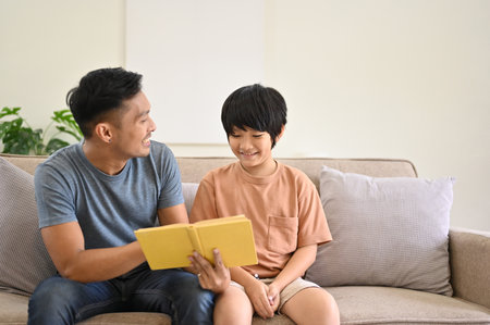Happy and kind Asian dad is talking and telling a story to his son on a sofa in the living room. family happy time conceptの写真素材