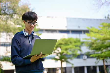 Smart and happy young Asian male college student using his portable laptop in the university park.の写真素材