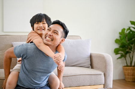 Joyful and happy Asian dad playing with his little son in the living room, piggyback, playing flying airplane, spending fun time together at home.の写真素材
