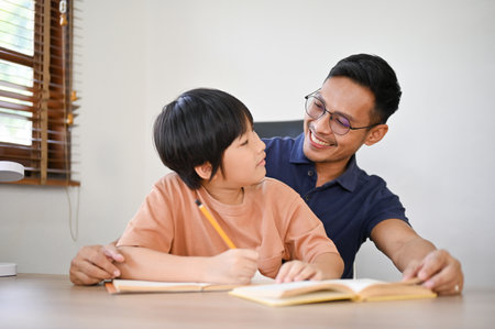 Confused and curious young little son asking a question while his dad is teaching and helping him do his homework.の写真素材