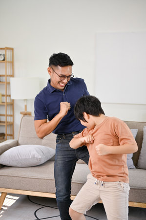 Cheerful and playful Asian dad and little son enjoying dancing in the living room together, having fun family time, happy single dad and son.の写真素材