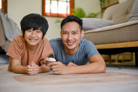 Happy and smiling Asian dad and son laying on the living room floor together, spending fun time on the weekend together.の写真素材