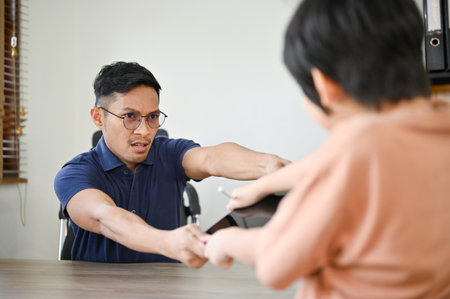 Angry Asian dad taking out a tablet from his son, having tablet battle fight. kid's computer and internet addictionの写真素材