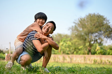 Smiling and happy Asian dad playing with his son in the backyard while carrying him on his back. piggyback pose. happy family and single dad conceptの写真素材